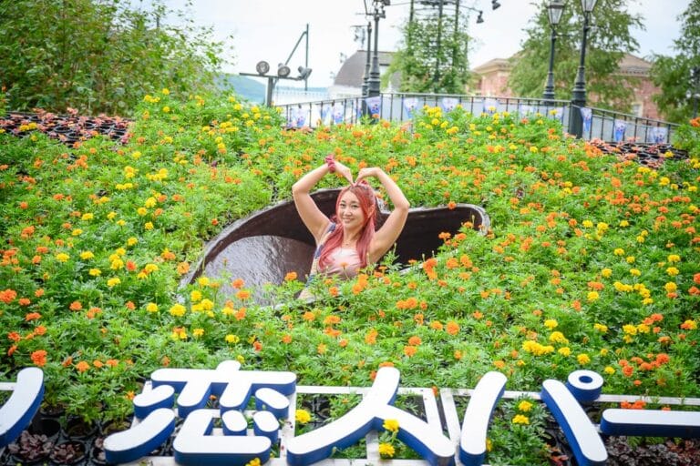 日本札幌-白色戀人觀光工廠｜女子，花叢，花壇，心型洞口，綠葉，黃橘色花朵，藍色日文字，戶外景觀。