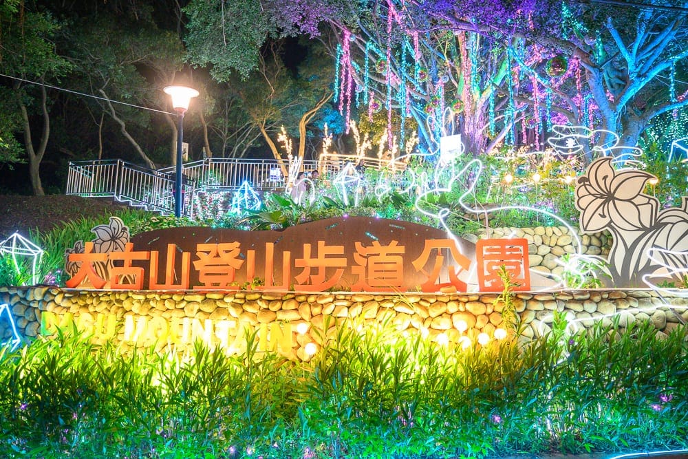 桃園大古山步道夏日繽紛派對完整攻略|夜間燈海步道玩法解析 10 桃園大古山步道夏日繽紛派對|夜間公園,大坑山登山步道公園招牌,石砌矮牆,草叢,樹木,七彩燈飾,燈桿,階梯扶手