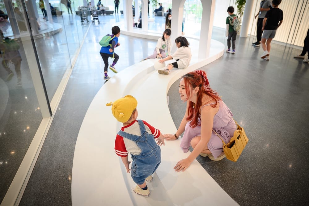 桃園市立兒童美術館｜室內，白色弧形矮牆，女性，幼童，孩童，灰色地板，玻璃帷幕