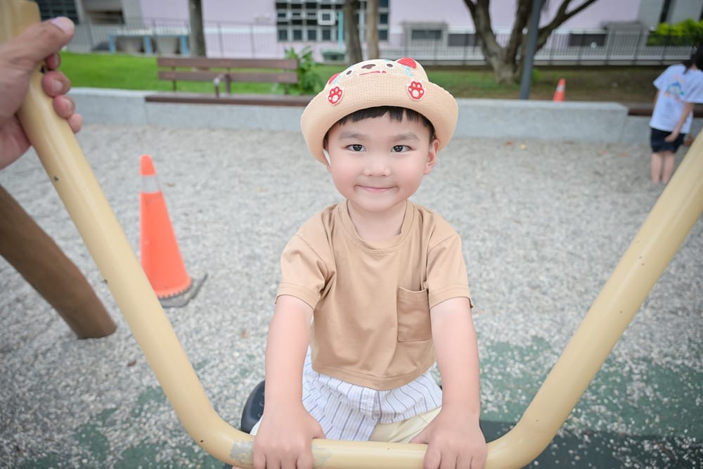 桃園中壢光明公園｜小男孩，帽子，遊樂場，欄杆，碎石地，三角錐，綠樹，戶外，直視鏡頭