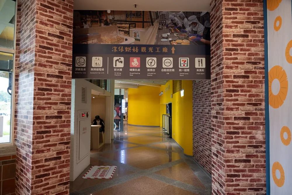 台南關廟服務區赤壁茶寮完整指南|竹牆茶品與農特產選購攻略 11 台南關廟服務區赤壁茶寮|室內、磚牆、告示牌、走廊、黃色牆面。仿紅磚柱子夾著走廊入口,上方懸掛指標牌,標示導覽與設施圖示,通道