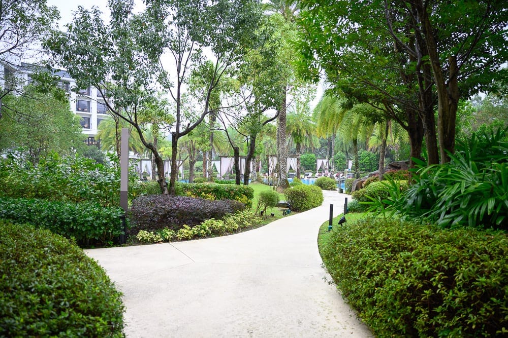 桃園威斯汀酒店 The Westin Tashee Resort 完整指南|親子設施與住宿體驗 7 桃園威斯汀酒店|水泥步道,草皮,灌木叢,綠樹,建築,戶外。白色彎曲步道貫穿綠意盎然的庭園,兩側修剪整齊的灌木與高大樹