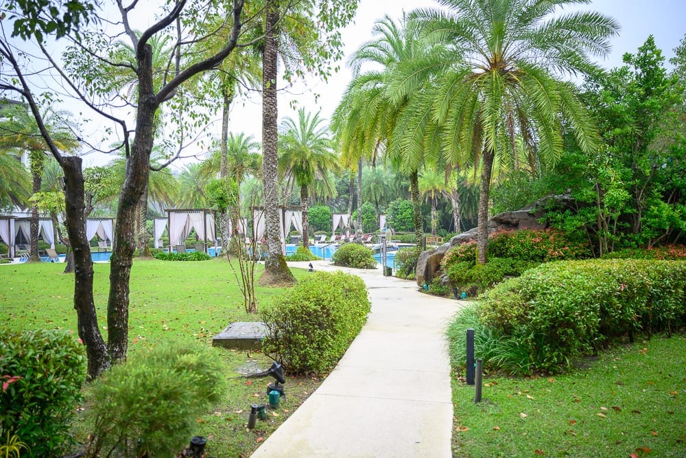 桃園威斯汀酒店 The Westin Tashee Resort 完整指南|親子設施與住宿體驗 10 桃園威斯汀酒店|綠地、棕櫚樹、步道、泳池、涼亭,戶外度假村的花園景致,白色石板路延伸向茂密樹叢,兩側為修剪整齊的灌木