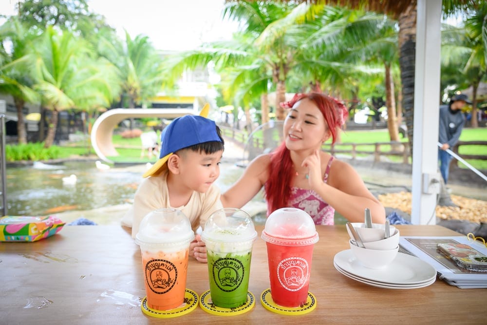泰國芭達雅 Pa Boon Café 5 親子景點完整指南|動物餵食與園林造景玩法解析 11 泰國芭達雅Paboon cafe|室內、木桌、飲料、塑膠杯、男孩、女子、水池、棕櫚樹