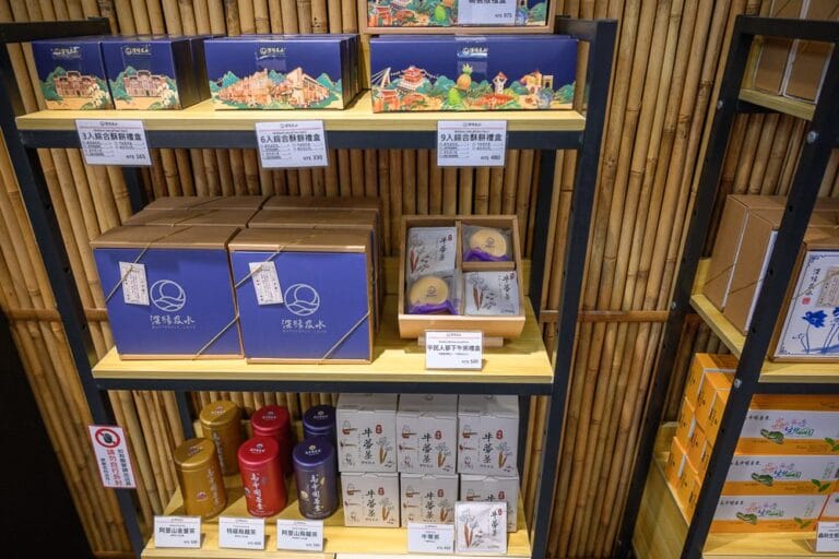 台南關廟服務區赤壁茶寮｜室內、層架、禮盒、茶葉罐、竹牆，木製層架上陳列著藍色禮盒、白色茶葉罐與黃色茶包，背景為垂直排列的竹片