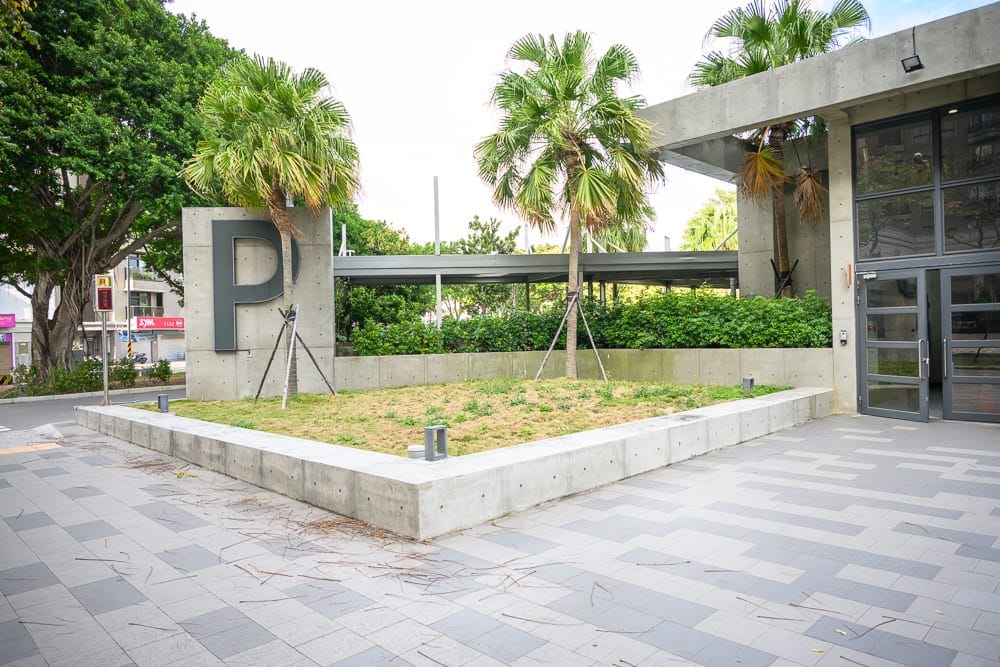 桃園文化兒童駕駛公園｜清水混凝土建築外，大片P字招牌，高聳棕櫚樹，綠色草皮花圃，灰階磁磚廣場鋪面，落地玻璃門，廊道結構。