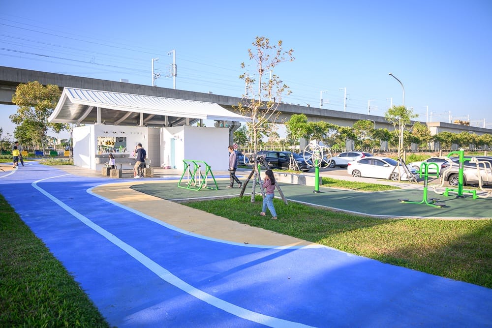 彰化熊趣米公園｜戶外公園、藍色跑道、白色建物、健身器材、停車場、高架橋、草地、行人。
