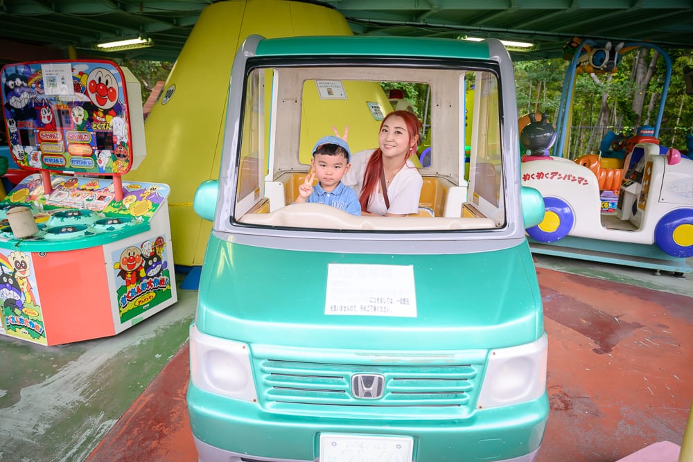日本福岡-福岡市動植物園｜綠色玩具車，遊樂場，婦人，男孩，遊戲機台，屋頂結構，紅磚地面
