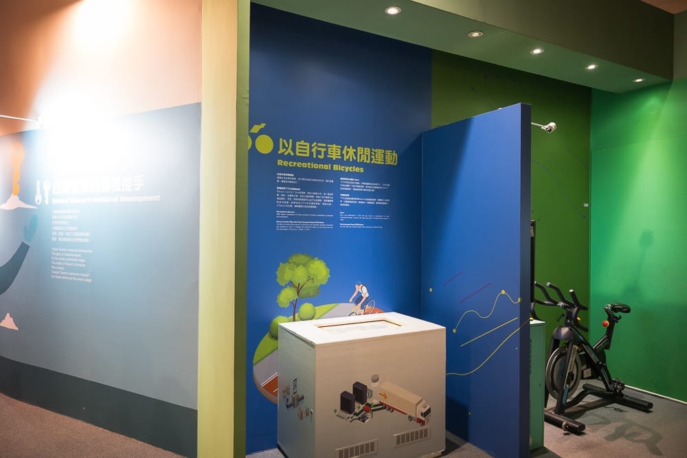 高雄國立科學工藝博物館完整攻略|親子展區與特展玩法解析 8 高雄國立科學工藝博物館|室內、展場、牆面、文字、圖解、白色方桌、黑色健身車、黃藍綠色牆面,天花板嵌燈照射藍色牆面,展示自行車
