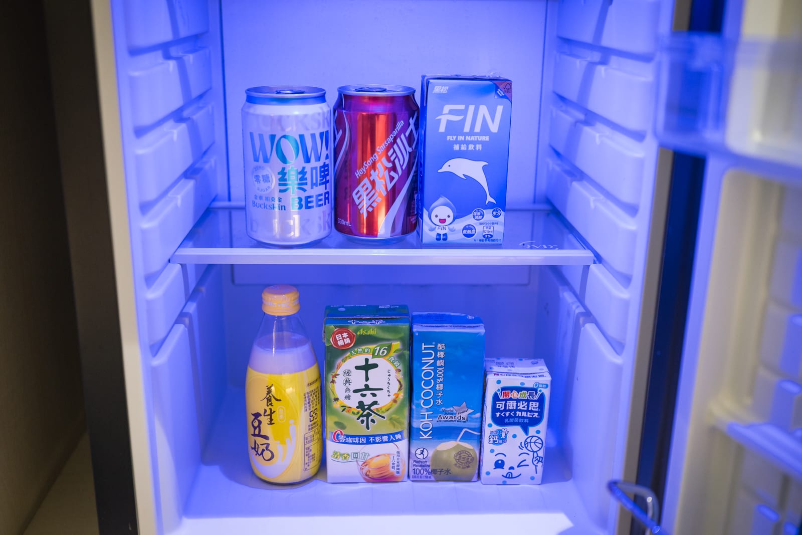 宜蘭凱渡廣場酒店｜冰箱，內部，飲料罐，鋁罐，紙盒裝飲料，塑膠瓶，藍色燈光。冰箱內部擺放多款鋁罐與紙盒裝飲料，藍色冷光照
