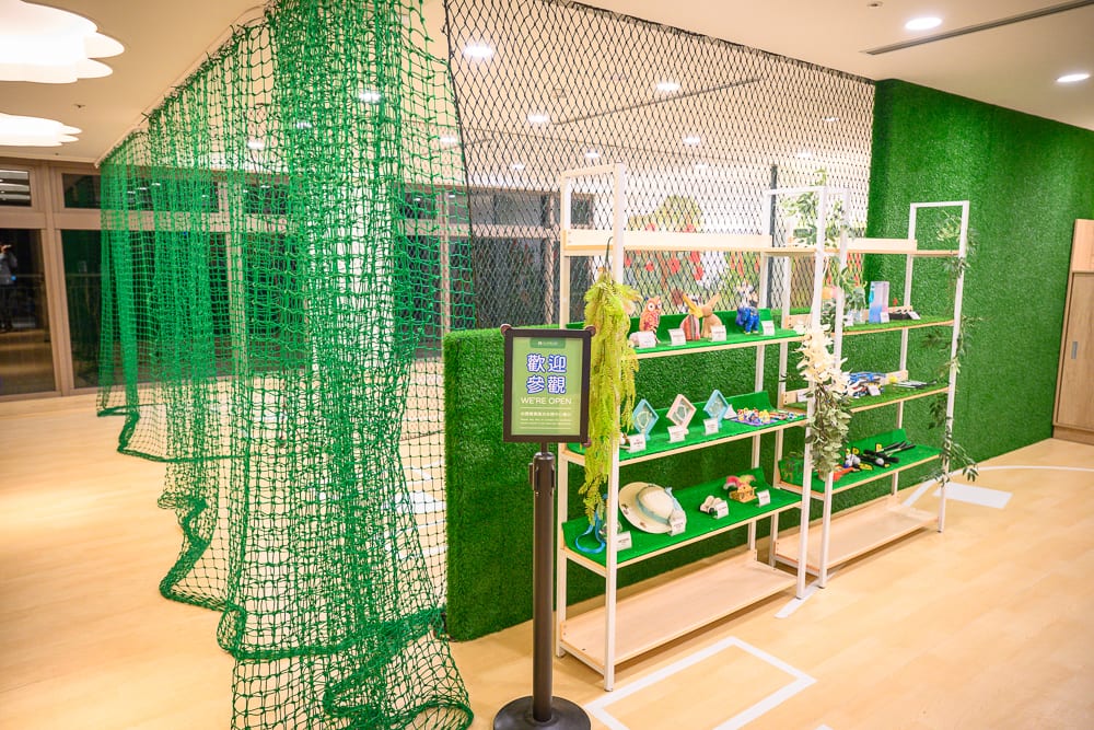桃園名人堂花園飯店｜室內，綠色網子，陳列架，草皮牆，展示品，招牌，木地板。室內空間有綠色防護網垂掛，旁邊立著擺滿展示品的