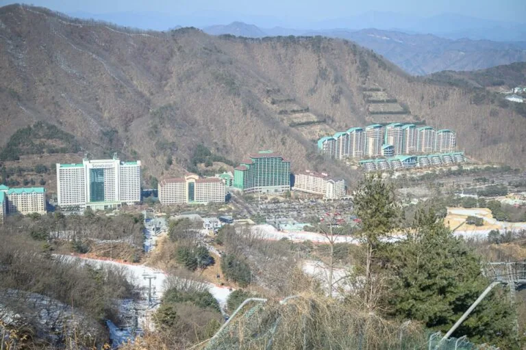 韓國首爾維瓦爾地渡假村冰雪王國｜山脈、渡假村、高樓大廈、樹林、雪道、纜車，遠山層疊，山谷間座落多棟大型飯店建築，前方鋪設零星殘雪的斜