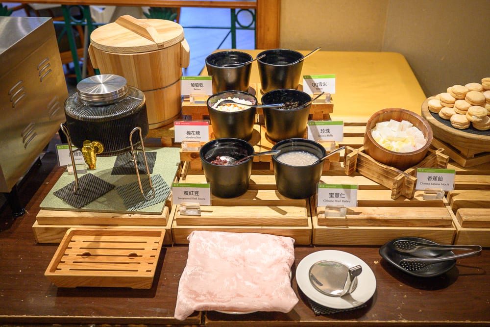 新竹煙波大飯店 新竹湖濱館完整攻略|餐飲設施與親子體驗指南 8 新竹煙波湖濱館|料理,木架,黑色碗,白色標籤,圓形容器,粉紅毛巾,室內桌面。木製架上整齊排列著多個黑色碗,內裝甜品配