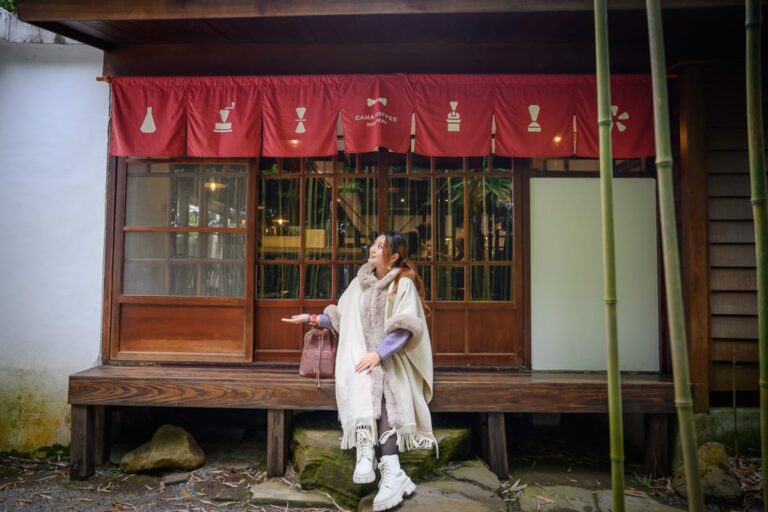 台北豆留森林｜木屋、竹林、女子、紅布簾、木造窗框、長凳。長髮女子身穿白色毛呢披肩與白靴，坐在木造店面門口的長凳上，