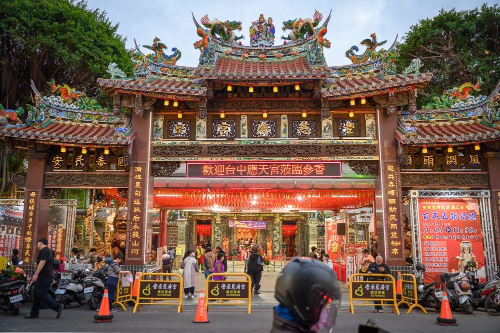 台中豐原廟東夜市完整攻略|慈濟宮老街小吃與必吃指南 7 台中廟東夜市|寺廟、牌樓、屋脊裝飾、紅燈籠、人群、機車、告示牌、街道。華麗傳統屋頂布滿雕刻與神像,下方懸掛電子跑馬
