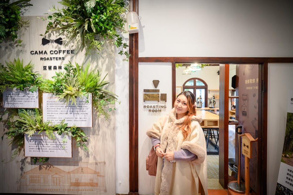 台北豆留森林完整攻略|日式老屋庭園咖啡與餐食體驗 7 台北豆留森林|室內、女性、披肩、牆面、植栽、招牌、門框。咖啡廳內,一名長髮女性身穿米色毛邊連帽披肩,站在白牆與木框