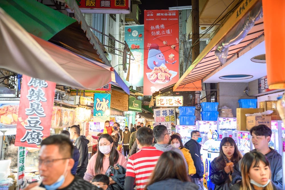 台中豐原廟東夜市完整攻略|慈濟宮老街小吃與必吃指南 6 台中廟東夜市|街道,夜市,人群,招牌,攤位,霓虹燈。夜間熱鬧市集街景,各色餐飲招牌與布條高掛,狹窄通道擠滿戴口罩的