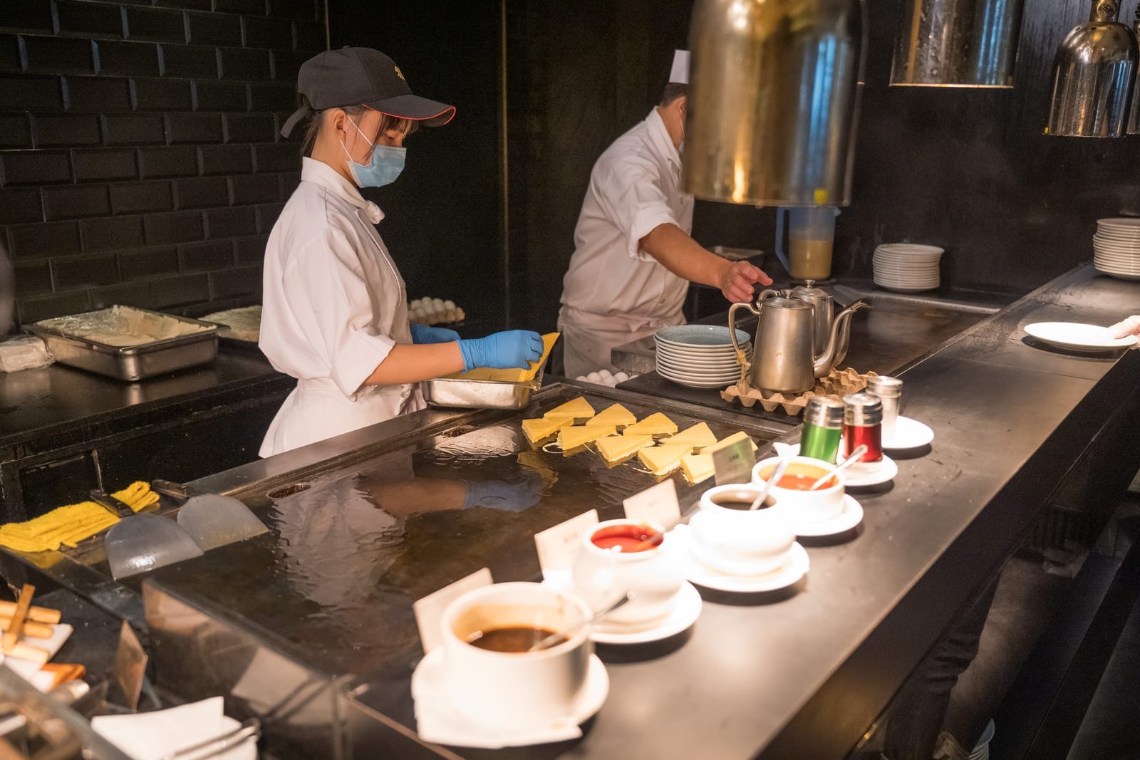 高雄漢來大飯店完整攻略|海景房、島語餐廳與交通住宿指南 12 高雄漢來飯店|室內,廚房,料理檯,廚師,煎台,三角形煎餅,醬料碗,金屬茶壺,戴口罩廚師