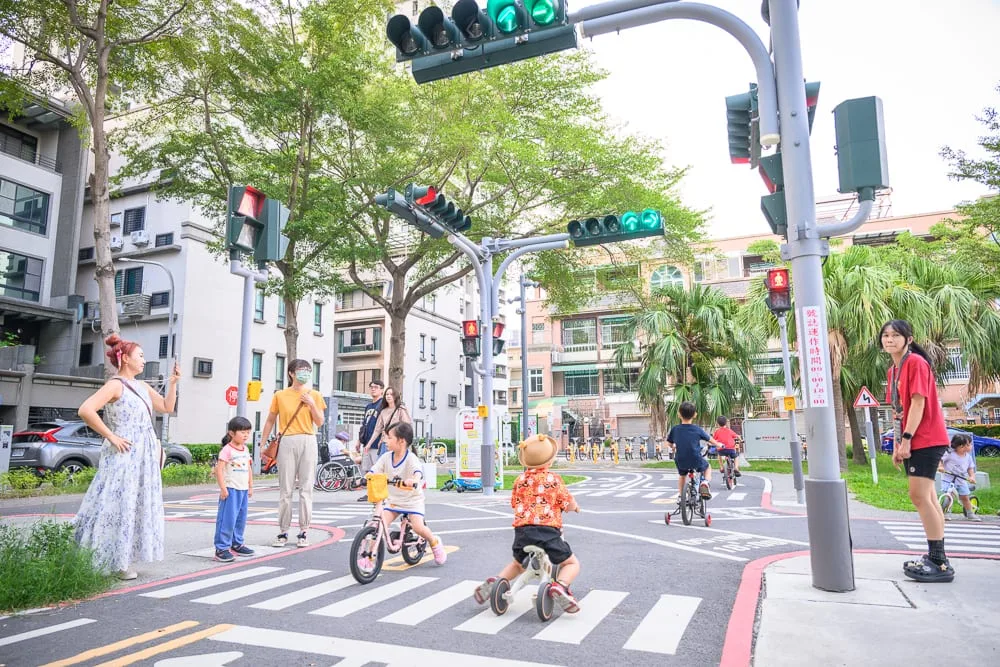 台南光賢交通公園｜街道，紅綠燈，斑馬線，幼童，滑步車，行人，樹木，住宅大樓，大人，交通號誌。戶外道路場景中，多位孩童騎