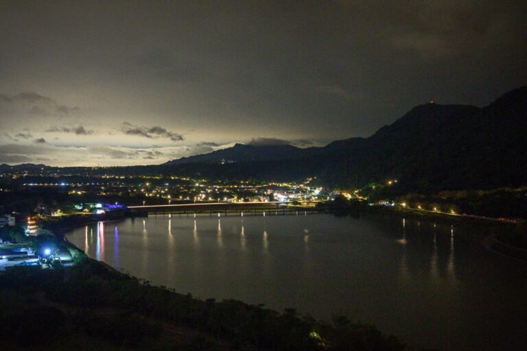 桃園福華石門水庫｜夜幕下的水庫，水面，橋，遠方山脈，燈光，雲層，低角度夜景構圖呈現水色倒影。