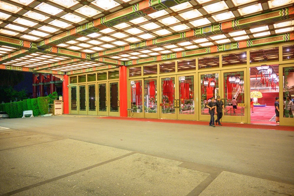 台北圓山大飯店完整攻略|宮殿建築外觀與密道體驗解析 13 台北圓山大飯店|建築外廊,大型方格頂棚,玻璃落地門,紅柱,瀝青車道,穿制服人員,燈飾