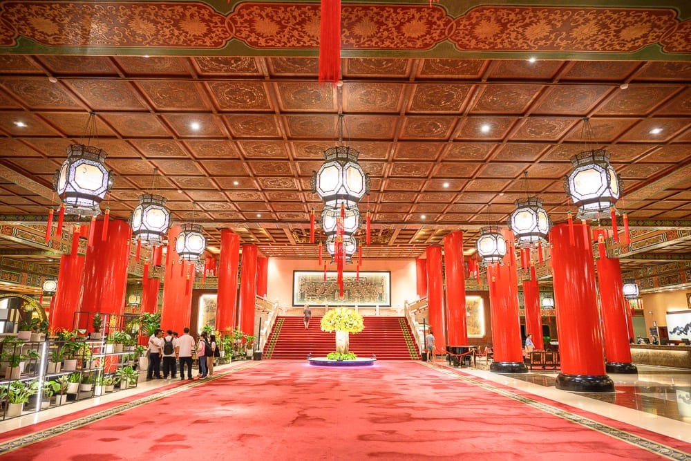 台北圓山大飯店完整攻略|宮殿建築外觀與密道體驗解析 9 台北圓山大飯店|室內、紅柱、宮燈、地毯、樓梯、人群,木格紋天花板懸掛多盞八角宮燈,兩側排列粗大朱紅圓柱,地面鋪設大片
