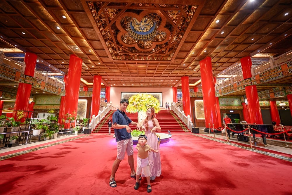 台北圓山大飯店完整攻略|宮殿建築外觀與密道體驗解析 8 台北圓山大飯店|室內、紅柱、地毯、樓梯、人物、吊燈、天井。宏偉大廳鋪設大片紅色地毯,粗大紅柱支撐木造格狀天花板,中央