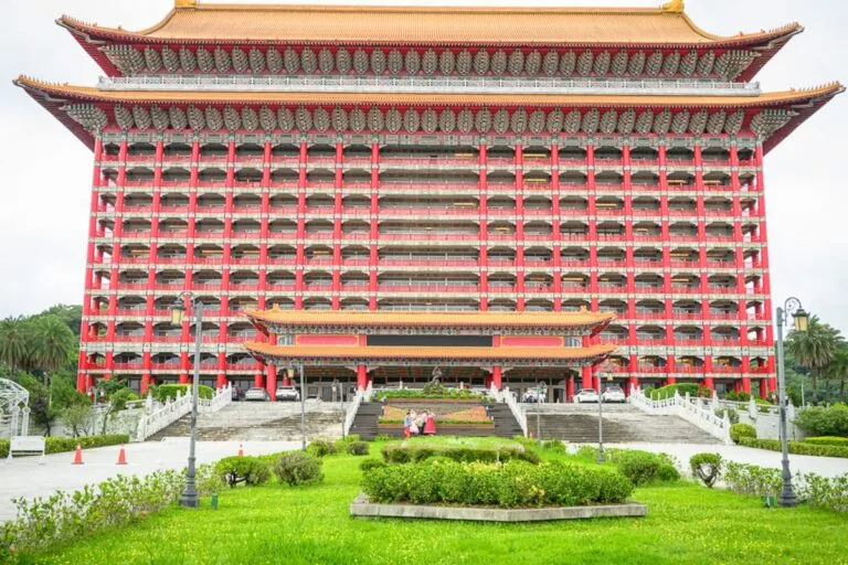台北圓山大飯店完整攻略|宮殿建築外觀與密道體驗解析 10 台北圓山大飯店|飯店、建築、廣場、階梯、草坪,巨大紅柱金瓦的宮殿式高樓巍峨聳立,正面多層陽台與斗拱排列整齊,前方設有