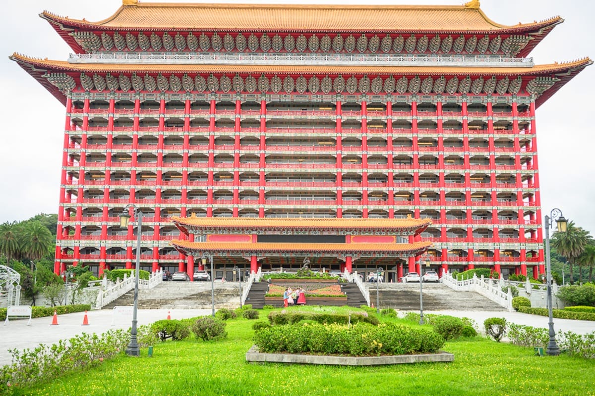 台北圓山大飯店完整攻略|宮殿建築外觀與密道體驗解析 1 台北圓山大飯店|飯店、建築、廣場、階梯、草坪,巨大紅柱金瓦的宮殿式高樓巍峨聳立,正面多層陽台與斗拱排列整齊,前方設有