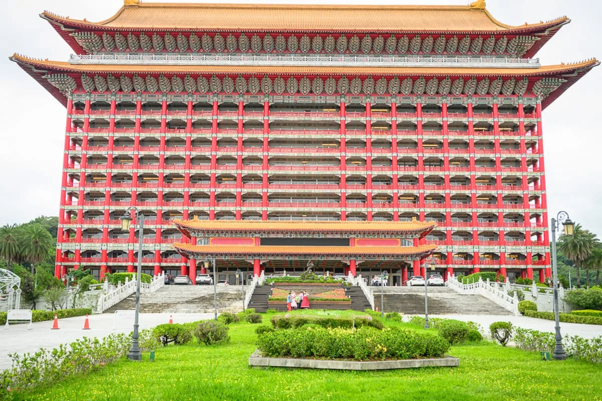 台北圓山大飯店完整攻略|宮殿建築外觀與密道體驗解析 1 台北圓山大飯店|飯店、建築、廣場、階梯、草坪,巨大紅柱金瓦的宮殿式高樓巍峨聳立,正面多層陽台與斗拱排列整齊,前方設有