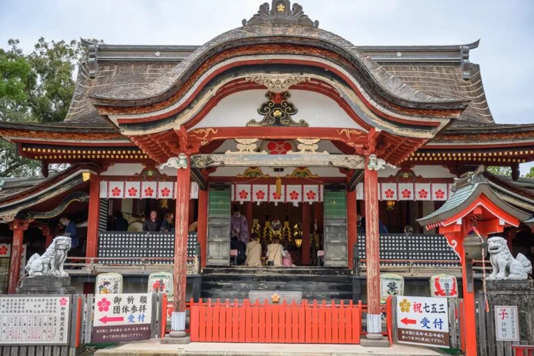 日本九州戀木神社心型御守完整攻略|戀愛祈願與池塘庭園玩法解析 5 日本九州-戀木神社|寺廟、神社、屋頂、木柱、石獅、燈籠、階梯、人群,紅白色調的日式傳統建築外觀,正殿前立著圍欄與指示牌,