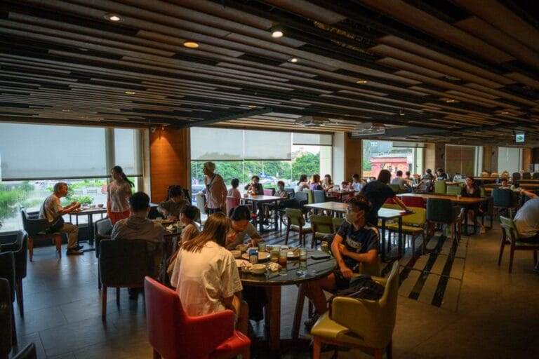 新北薆悅酒店野柳渡假館完整攻略|兒童遊樂設施與漁人餐廳住宿指南 18 新北薆悅酒店|室內,餐廳,桌椅,人群,吊頂天花板,大片玻璃窗,盆栽。餐廳內部光線明亮,擺放著多張圓桌與方桌,座位坐