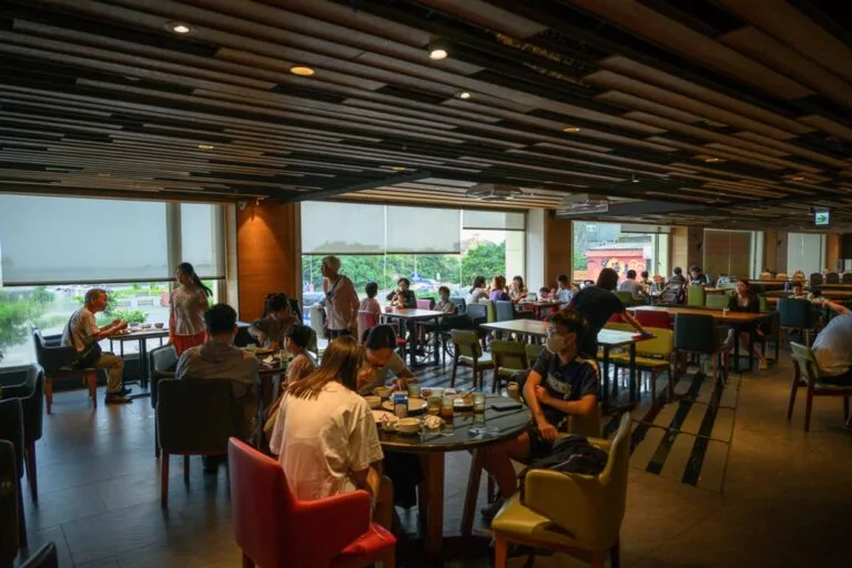 新北薆悅酒店野柳渡假館完整攻略|兒童遊樂設施與漁人餐廳住宿指南 17 新北薆悅酒店|室內,餐廳,桌椅,人群,吊頂天花板,大片玻璃窗,盆栽。餐廳內部光線明亮,擺放著多張圓桌與方桌,座位坐