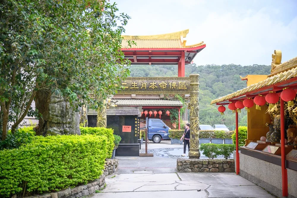 桃園威天宮｜寺廟、紅柱、金頂、樹木、綠叢、紅燈籠，中式建築廣場停放貨車，行人走過石板地。