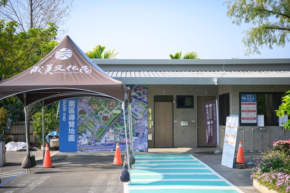 彰化成美文化園｜棕色帳篷、園區導覽地圖、灰色建物、入口通道、橘色三角錐、立牌、花圃，戶外廣場有藍綠色斑馬線與多個指引