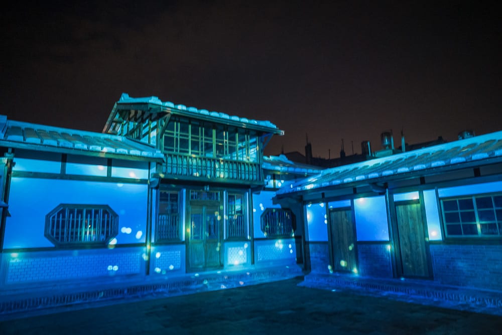台南月之美術館｜傳統木造建築群，院落，門窗，藍色光影投射，夜空，地面。建築外牆被藍色燈光照亮，牆面佈滿白色光斑。