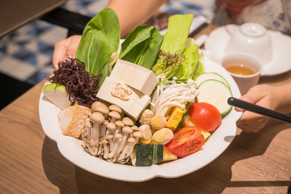 高雄福華大飯店完整攻略|屋頂泳池、早餐自助與尊爵房型解析 7 高雄福華飯店|室內、料理,木桌上擺著一個白色大圓盤,盤內盛裝鴻喜菇、金針菇、青江菜、番茄、南瓜、豆腐、海藻與櫛瓜,