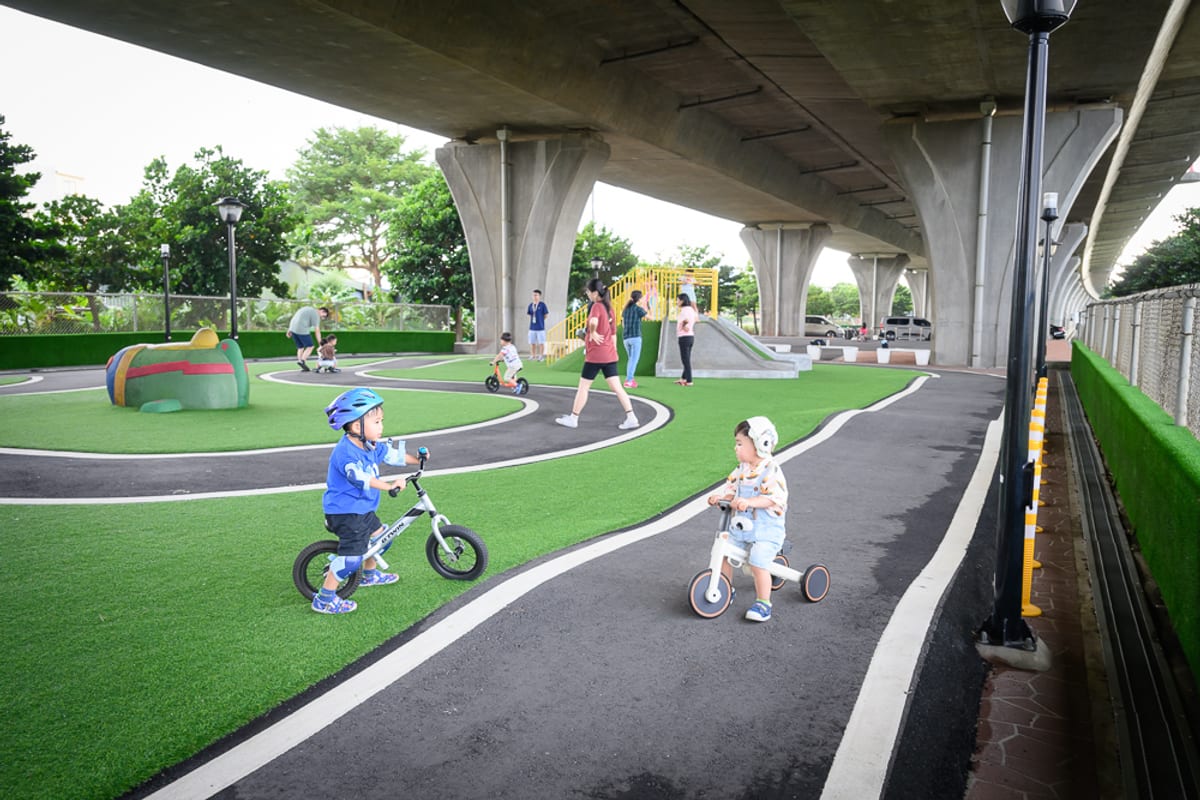 苗栗竹南滑步車公園｜高架橋下空間，人工草皮，滑步車道，幼童，家長，遊樂設施，路燈。兩名幼童騎著滑步車在黑色跑道上，四周鋪
