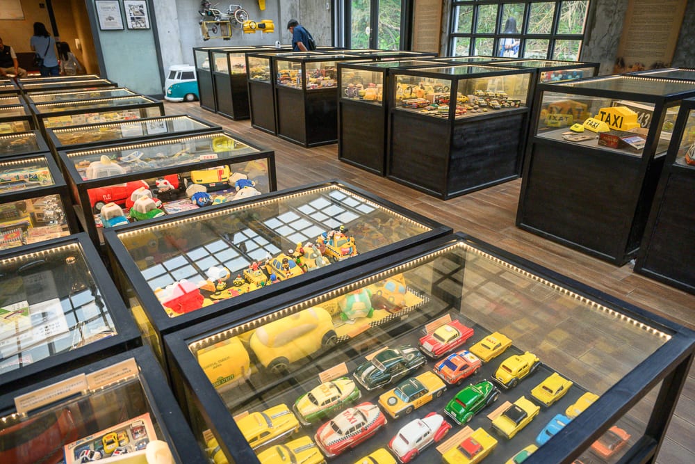 宜蘭計程車博物館｜室內、展覽館、展示櫃、玩具車、模型車、木地板。室內空間擺放多排黑色玻璃展示櫃，櫃內陳列各種顏色與造型的小型玩具車與模型車，玻璃邊緣帶有燈條照明，地板為木質。