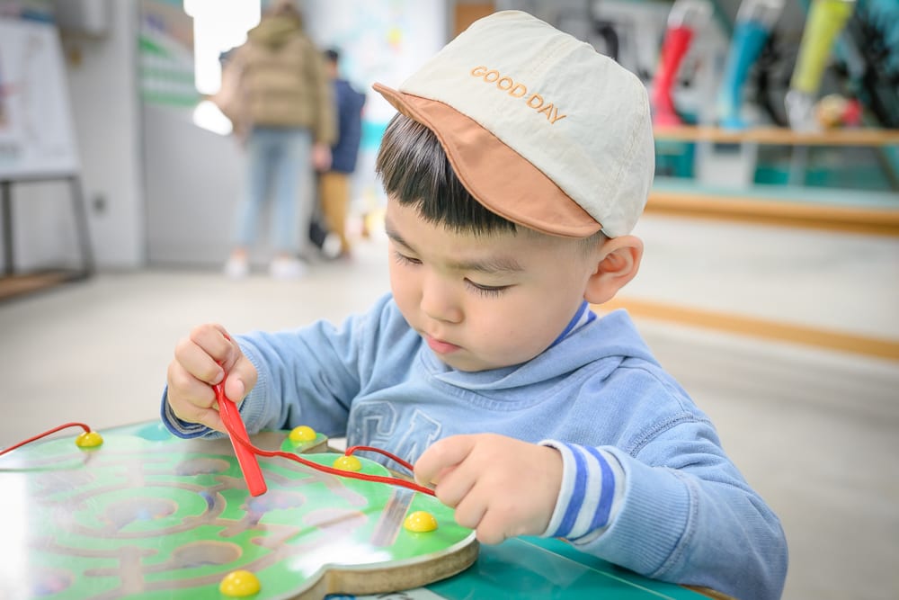 彰化台灣手套博物館｜室內、孩童、鴨舌帽、益智玩具、桌面。小男孩戴著米色與棕色拼接的鴨舌帽，穿著藍色長袖上衣，正低頭專注地