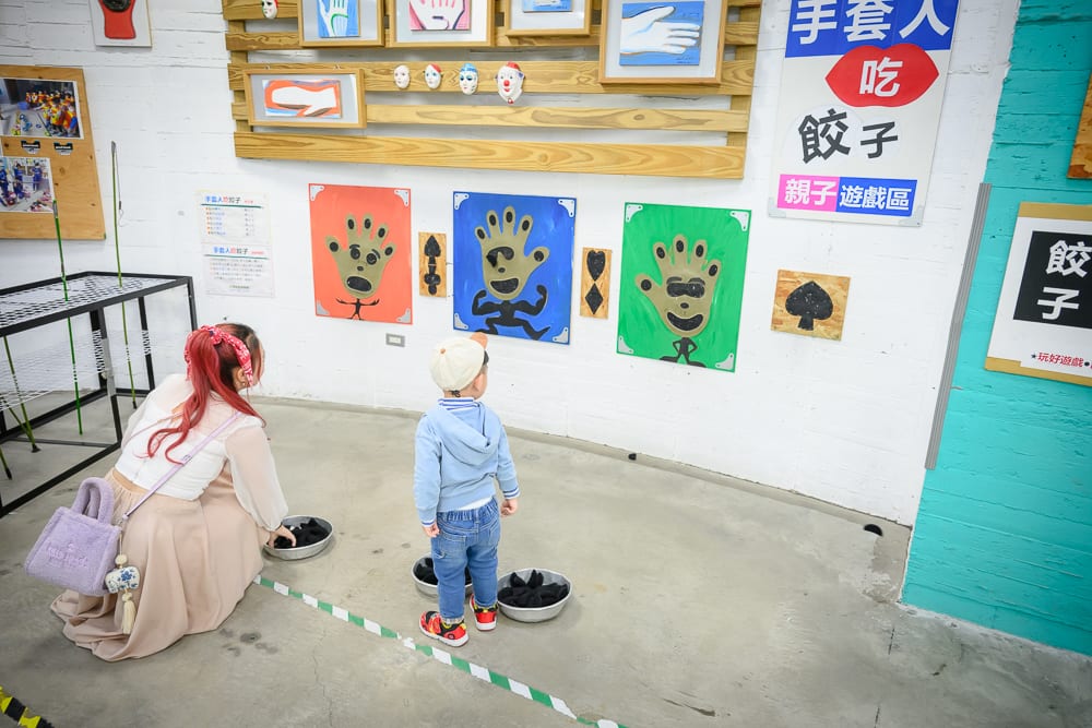 彰化台灣手套博物館｜室內、牆面、畫作、大人、小孩、鐵盆，紅髮女子半蹲在地，戴帽男童站立前方，牆面懸掛彩色手掌圖案與中文字