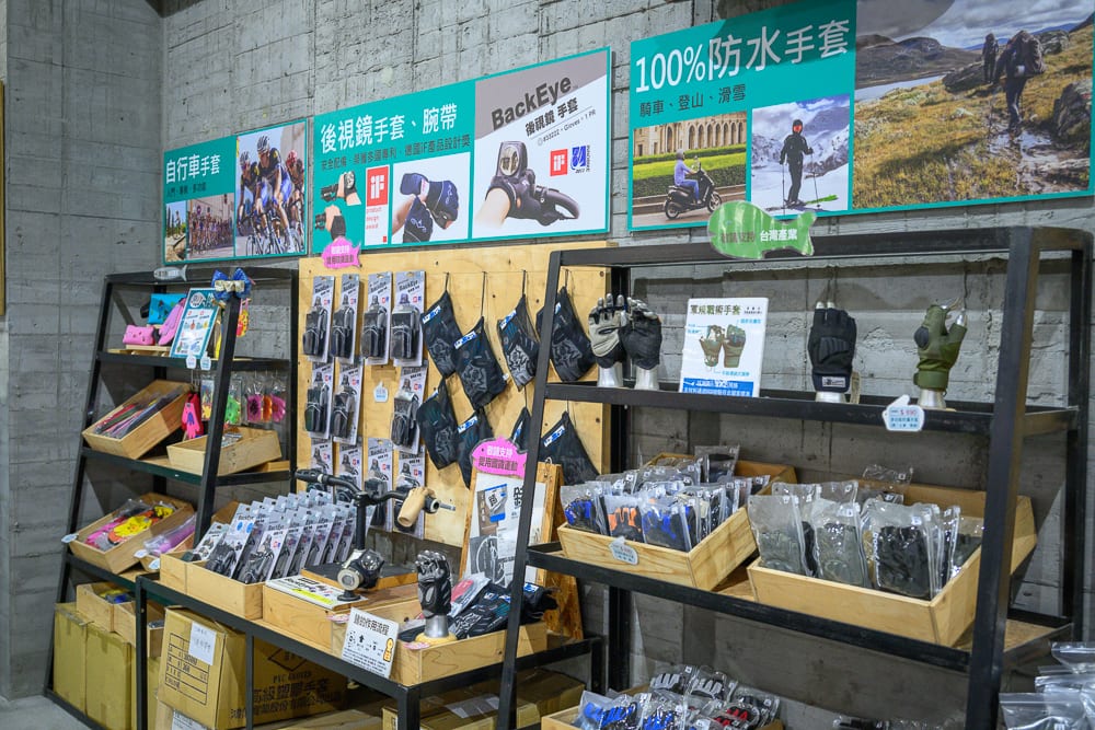 彰化台灣手套博物館｜室內、金屬架、木箱、商品展示架、手套、吊牌、宣傳海報、水泥牆。層架陳列多款防水與運動手套，牆面懸掛圖