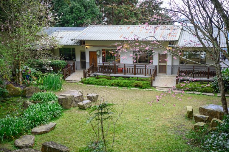嘉義寒溪呢｜平房建築、草地、櫻花、木造走廊、石塊、庭園，灰瓦白牆平房前有片綠草地與石塊造景，四周環繞著茂密樹木與