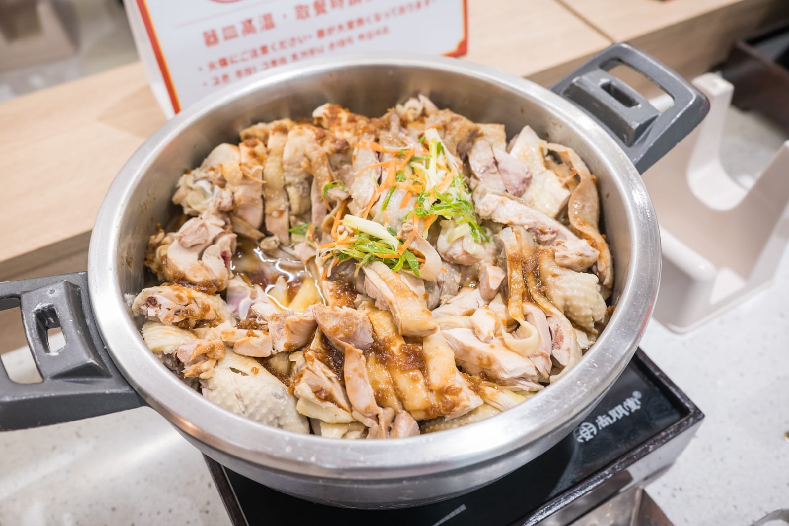新竹六福莊關西｜料理，不鏽鋼湯鍋，切片雞肉，醬汁，蔥絲，胡蘿蔔絲，電磁爐，餐廳自助吧。金屬雙耳鍋內盛裝切塊白斬雞，淋上深色醬汁並點綴蔬菜細絲，置於黑色發熱盤上。