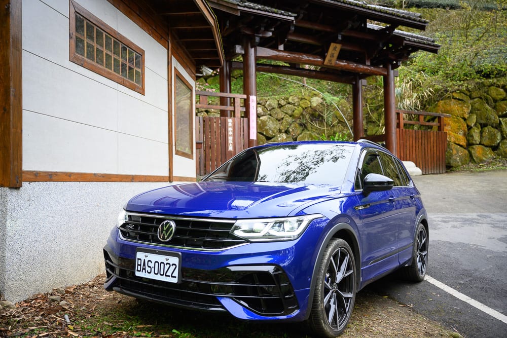 嘉義寒溪呢｜休旅車、車輛、建築、木造門廊、石牆、山坡。藍色福斯休旅車停在日式木造建築與石牆旁，車身反射出環境光影