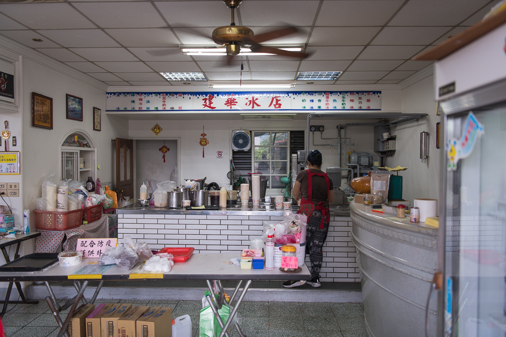 宜蘭建華冰店｜建華冰店，室內櫃檯、工作人員、冰品配料、桌椅、天花板吊扇。
