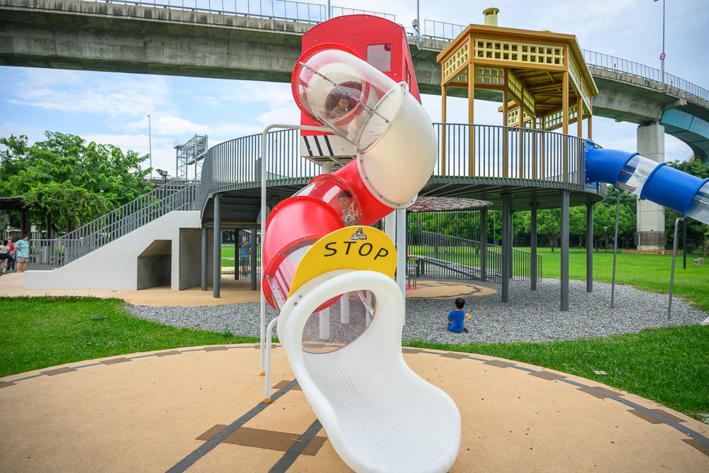 彰化景觀公園完整指南|兒童遊樂設施與高架橋下綠地玩法 13 彰化景觀公園|戶外公園,遊樂場,溜滑梯,高架橋,草地,欄杆,兒童。多元色彩的塑膠滑梯管道自高處延伸而下,下方鋪設碎