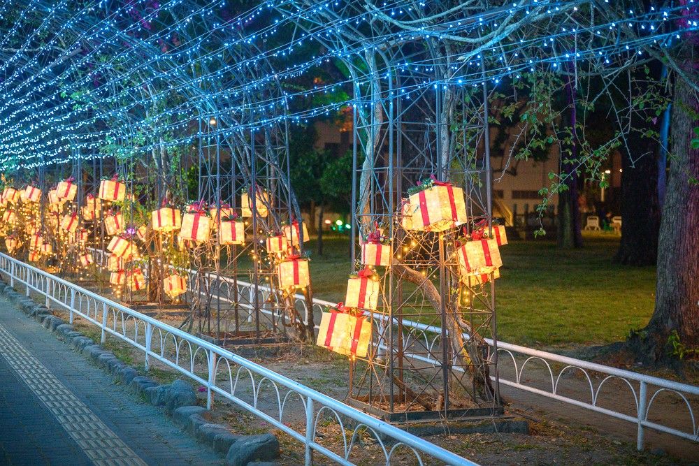 2026屏東聖誕節|屏東公園聖誕燈飾 11/6 亮燈:展演時間、泡泡遊行、慈鳳宮燈區、交通停車攻略 5 屏東公園步道旁一整排暖黃色禮物盒燈籠,上方是藍色燈串棚架