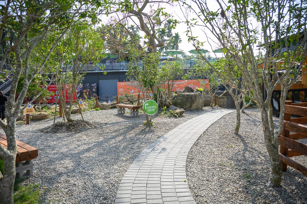 南投鹿芝谷生態景觀園區完整指南|餵羊、水豚與親子玩法 4 南投鹿芝谷|石子地庭園,彎曲石板步道,綠樹,木椅,指示牌,遠方建築。