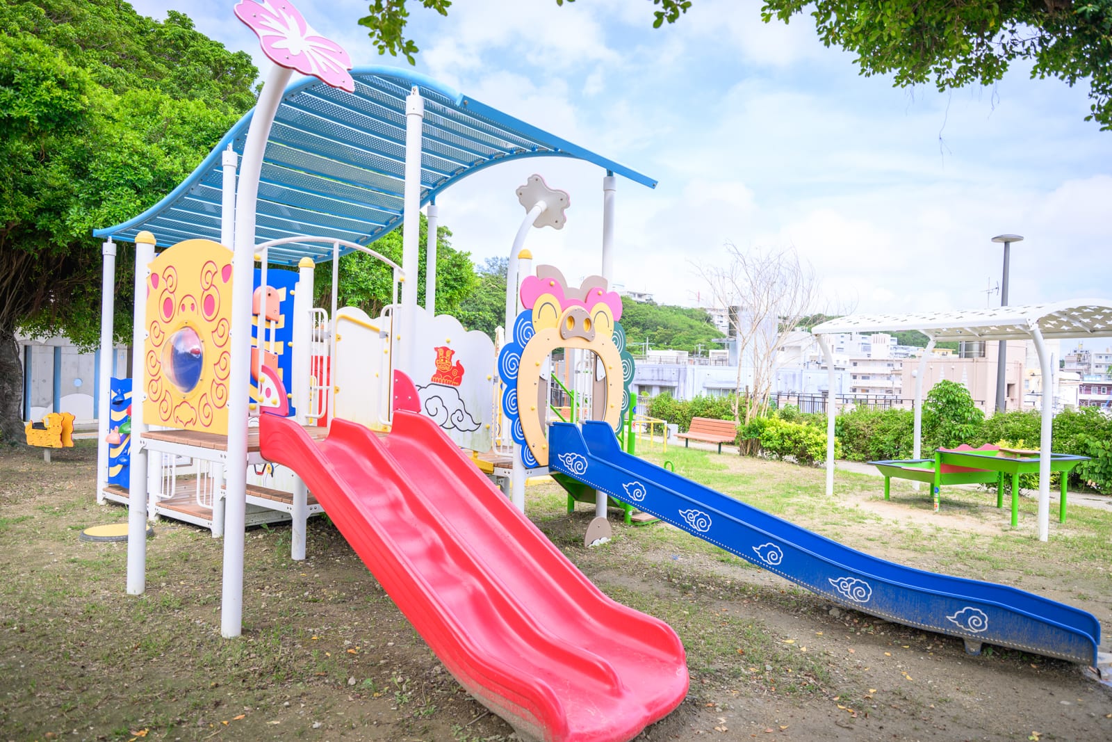 日本沖繩海軍壕公園完整指南|地下壕博物館與兒童遊樂場 9 日本沖繩海軍壕公園|戶外公園,遊樂設施,紅色滑梯,藍色滑梯,遮陽棚,草地,樹木,天空